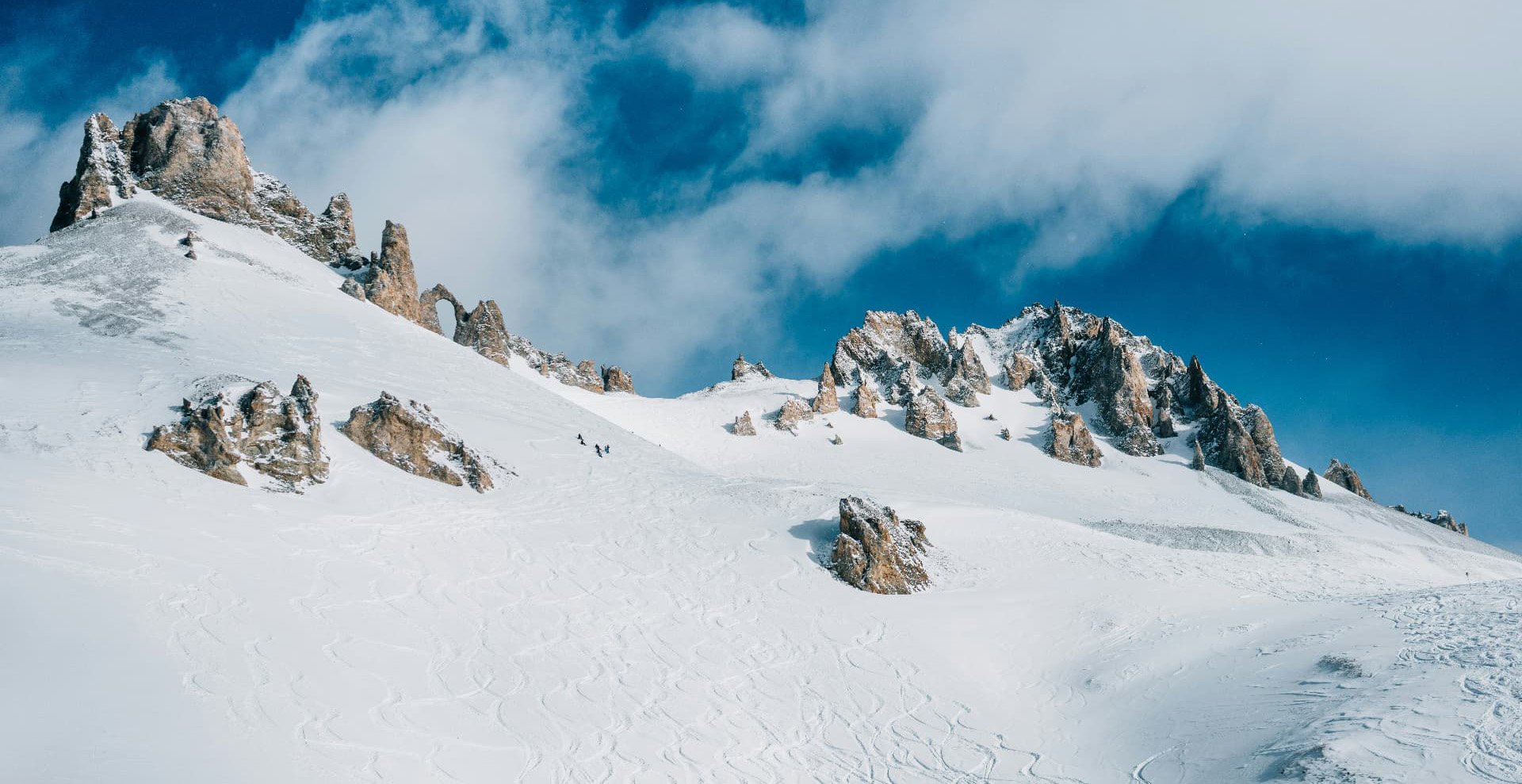 Skiers below the Eye of the Needle rock formation above Tignes